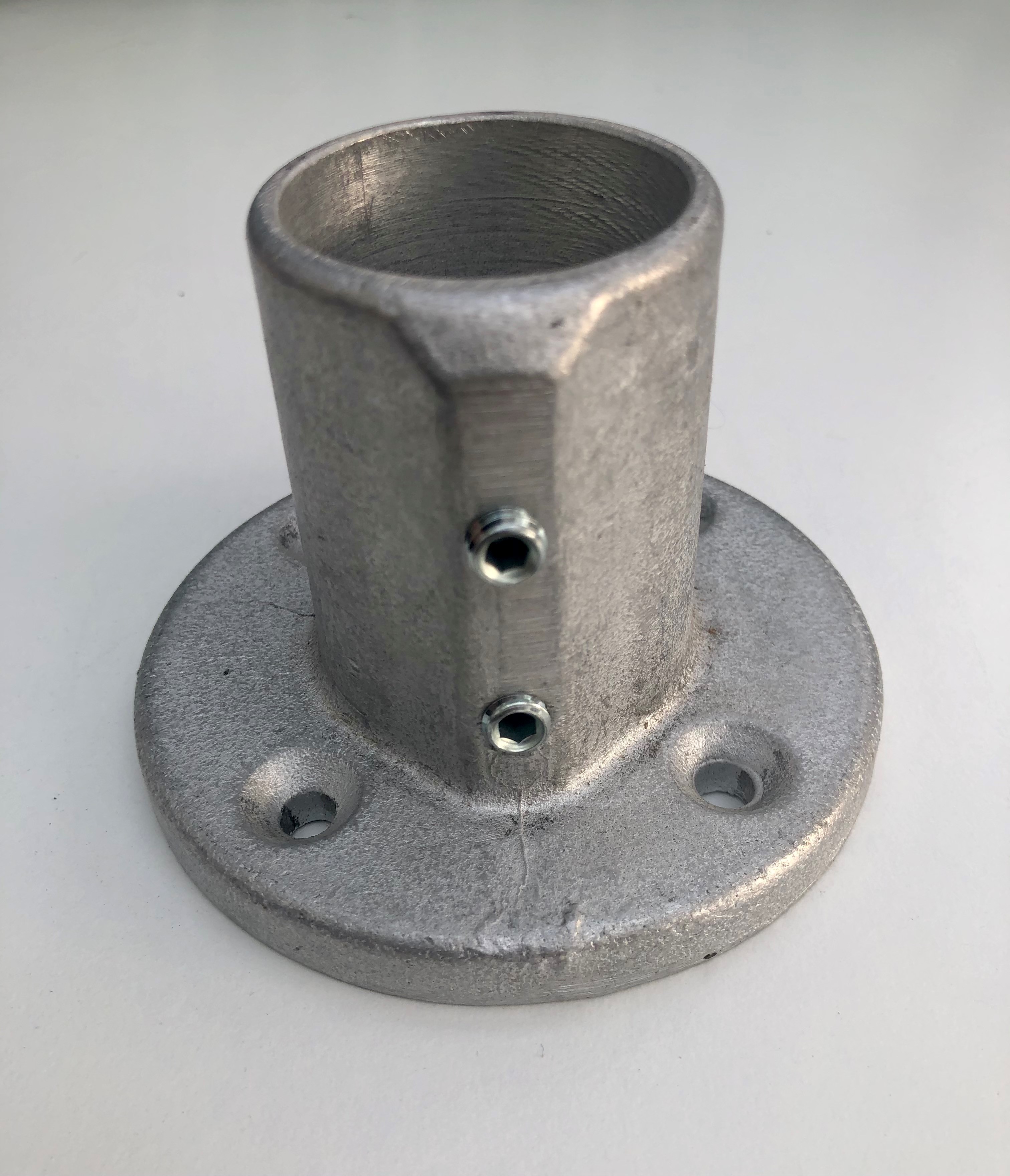 Silbergrauer, zylindrischer Metallflansch mit runder, flacher Basis und drei Montagelöchern. Der 40mm hohe Hohlzylinder besitzt zwei seitliche Innensechskantschrauben zur Rohrbefestigung. Robuster Verbinder.
